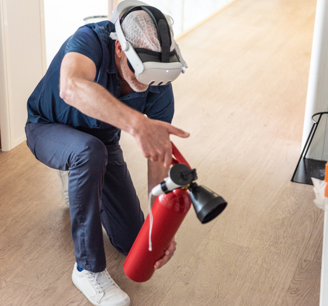Homme portant un casque de réalité virtuelle manipulant un extincteur rouge lors d'une formation incendie en VR