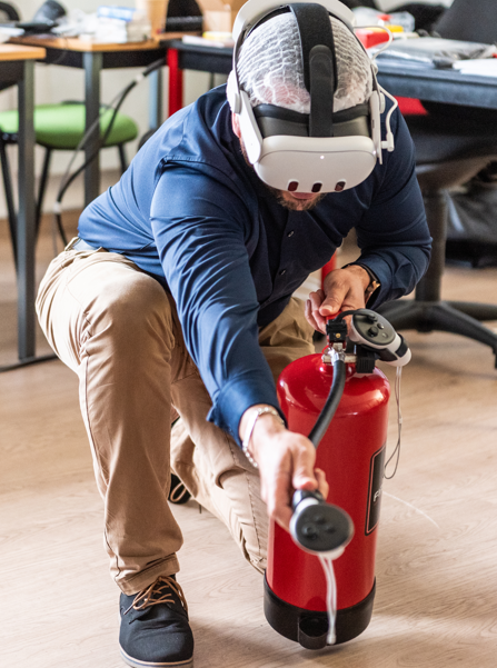 Personne portant un casque de réalité virtuelle manipulant un extincteur rouge lors d'une formation incendie en réalité virtuelle
