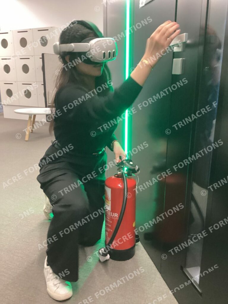 Stagiaire équipée d'un casque de réalité augmentée qui vérifie la chaleur d'une porte avant de l'ouvrir, extincteur à la main, formation incendie TRINACRE